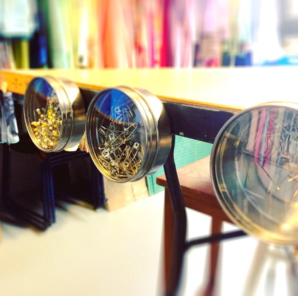 magnetic tins holding sewing pins, safety pins and needles, stuck to the edge of a wooden table